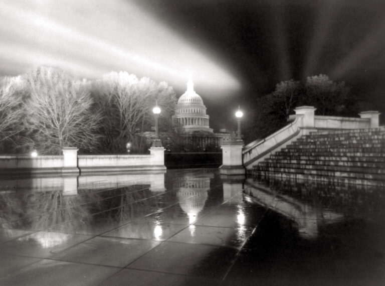 Night view of the U.S. Capitol in Washington, D.C., with reflective wet pavement and illuminated dome.