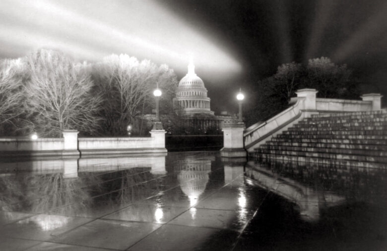 Night view of the U.S. Capitol in Washington, D.C., with reflective wet pavement and illuminated dome.